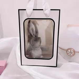 Kleine witte papieren geschenkzak met zwarte rand en doorzichtig venster voor bloemen en taart.