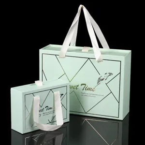 Set di scatole regalo a cassetto verdi con manici in nastro bianco e linee geometriche.