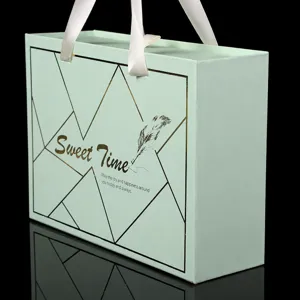 Scatola regalo verde menta creativa con manico in nastro bianco e linee geometriche dorate.
