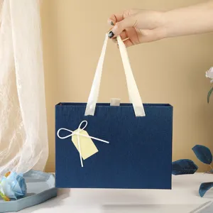 Boîte cadeau bleue avec poignées en ruban blanc et nœud décoratif pour fêtes et anniversaires.