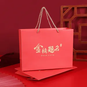 Sac cadeau en papier rouge avec texte doré, idéal pour les fêtes de graduation et cadeaux.