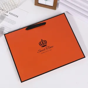 Orange paper gift bag with black ribbon handle and crown logo, perfect for clothing and gifts.