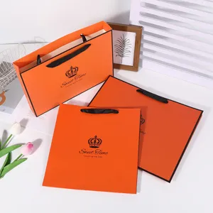Orange paper gift bag with black handles and crown logo, luxury boutique tote bag for retail.
