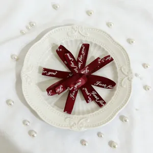 Fiocco in nastro bordeaux con testo dorato, ideale per confezioni regalo e decorazioni dettagliate.