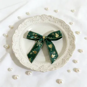 Fiocco in nastro natalizio verde con stampa dorata, presentato su piatto bianco con perle.