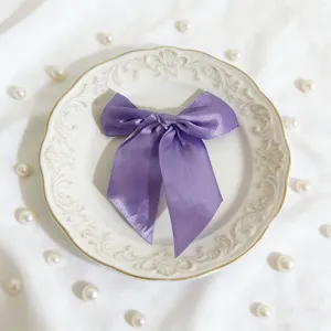 Dettaglio fiocco in raso viola, elegante fiocco decorativo su piatto bianco con perle.