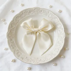 Dettaglio elegante fiocco in nastro di raso crema, perfetto per decorare scatole regalo.
