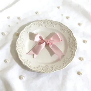 Primo piano di fiocco in nastro di satin rosa su piatto vintage decorativo con perle per scatole.