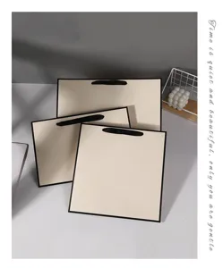 Minimalist beige paper gift bags with black handles, elegant packaging for retail and shopping.