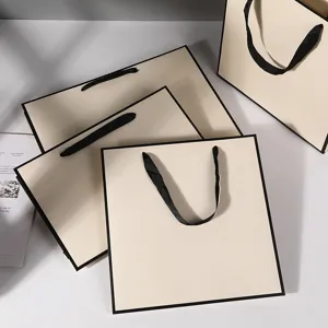 Minimalist beige gift bags with black borders and ribbon handles, ideal for clothing and retail.