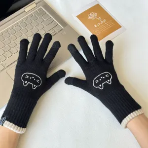 Close-up of black knitted winter gloves with cute cat embroidery and touch screen feature.