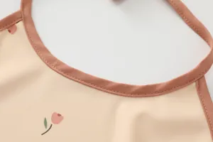 Detailed close-up shot of children's waterproof bib with cute tulip print and brown trim.