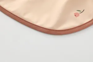 Detail shot of waterproof baby bib featuring neat brown piping and a cute cherry pattern print.