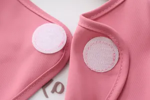 Kids waterproof bib detail shot, pink coverall fabric with secure velcro closure for daily feeding.