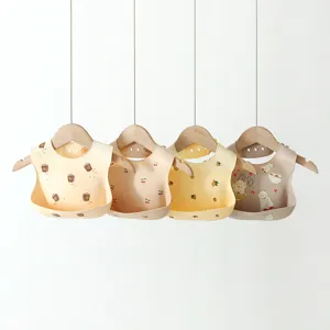 Detailed view of cute silicone baby bibs hanging on wooden hangers with various playful prints.
