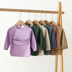 Waterproof long sleeve baby bibs in multi colors hanging on rack detail view with pockets