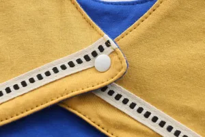 Gros plan sur les coutures et boutons-pression du bavoir bébé, texture coton doux.