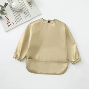 Vista detallada del babero impermeable de manga larga dorado para bebés durante las comidas.