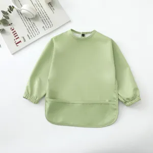 Detalle de babero impermeable de manga larga para bebé en verde claro, tela suave.