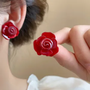 Nahaufnahme glänzender roter Rosenohrringe mit exklusivem mehrschichtigen Blumendesign.