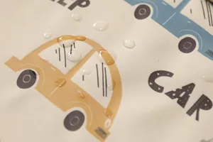 Close-up detail of baby waterproof PU feeding bib fabric showing water droplets and cars.