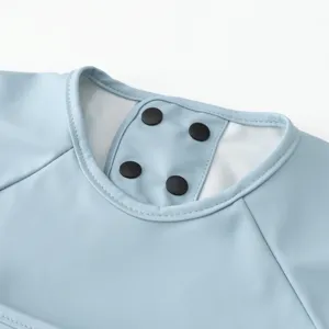 Close-up detail of light blue baby bib smock collar and black snap buttons, soft PU fabric.