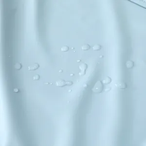 Waterproof fabric detail shot showing water droplets on soft light blue baby smock material.
