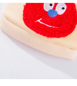 Pet clothing detail shot featuring a cute red plush cartoon monster on beige cotton fabric. Soft, cozy texture.