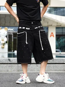 Primo piano di pantaloncini in denim nero da uomo con strass brillanti e bordi sfrangiati.