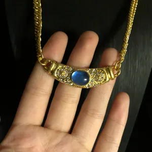 Detailed close-up of a vintage-style gold-plated blue rhinestone pendant necklace accessory.