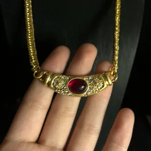 Close-up detail of vintage gold-plated necklace pendant with rhinestones and red stone.