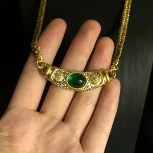 Close-up detail of vintage style gold-plated necklace with green gemstone and rhinestones.