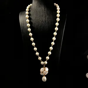 Detailed shot of long pearl necklace with mother-of-pearl flower pendant and gold-tone links.