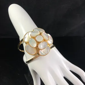 Elegant gold tone cuff bracelet featuring a mother of pearl camellia flower motif.