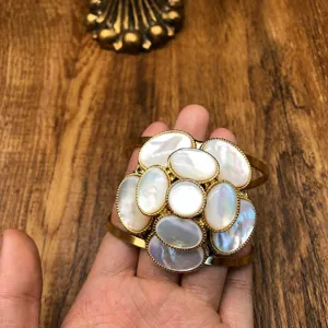 Close-up detail of luxury gold-tone mother-of-pearl floral cuff bracelet texture.