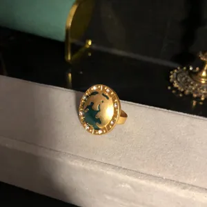 Gold-plated enamel earth ring detail close-up showing green continents and sparkling rhinestones.