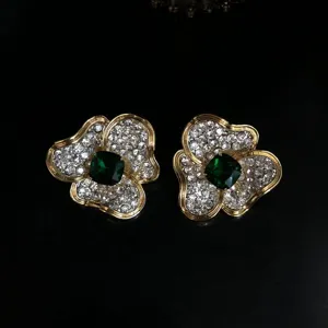 Gros plan de boucles d'oreilles florales vintage dorées avec strass et cristal vert.