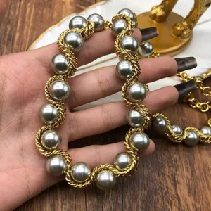 Primer plano detallado de un collar vintage con cadena dorada trenzada y perlas grises elegantes.