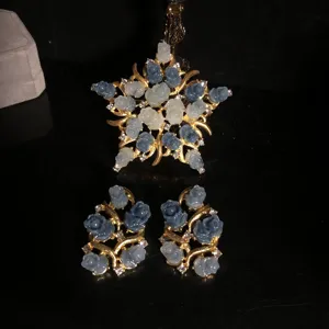 Detail of carved blue white rose pendant and earrings set with gold finish and sparkling stones.
