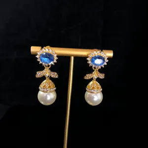 Close-up detail of vintage-style blue gemstone rhinestone pearl dangling earrings on gold stand