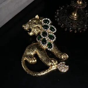 Vintage style gold lion brooch featuring green glass stones and sparkling rhinestones for details.