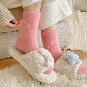 Gros-plan de chaussettes douillettes en peluche rose avec motif cœur et détails de pantoufles.
