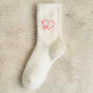 Gros plan détaillé de chaussettes en peluche blanche douillettes avec motif de cœur brodé.