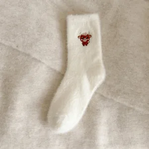 Gros plan de chaussettes douillettes blanches et duveteuses avec un joli motif de petit taureau.