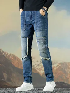 Jeans de mezclilla elásticos azules para hombre con patchwork y bordes deshilachados rústicos.