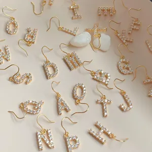 Nahaufnahme von zarten Gold Buchstaben Ohrringen mit glitzernden Zirkonia Steinen.