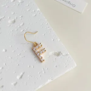 Nahaufnahme eines vergoldeten Zirkon-Buchstaben-Ohrrings auf strukturierter Platte.