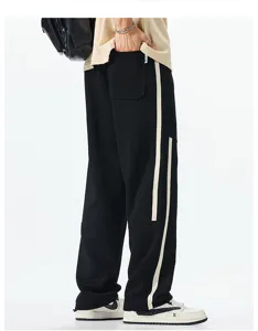 Detail view of black casual sweatpants with beige side stripes, loose fit and straight leg design.