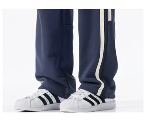 Detail view of casual loose straight-leg track pants with side stripes and sneakers.