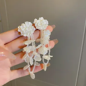 Vista dettagliata di orecchini lunghi con perle floreali bianche, stile elegante e fatato.